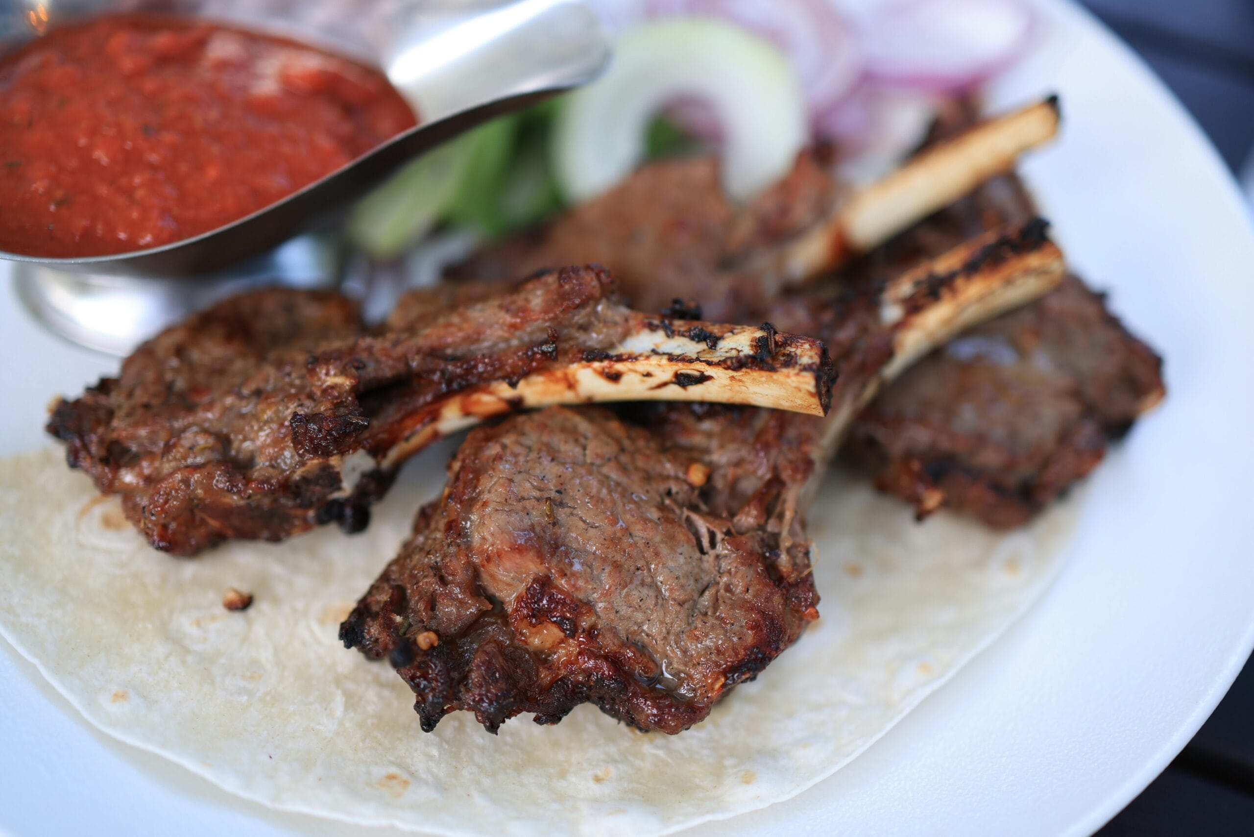 Close-up of juicy grilled lamb chops on a plate with sauce and vegetables, perfect for gourmet meals.
